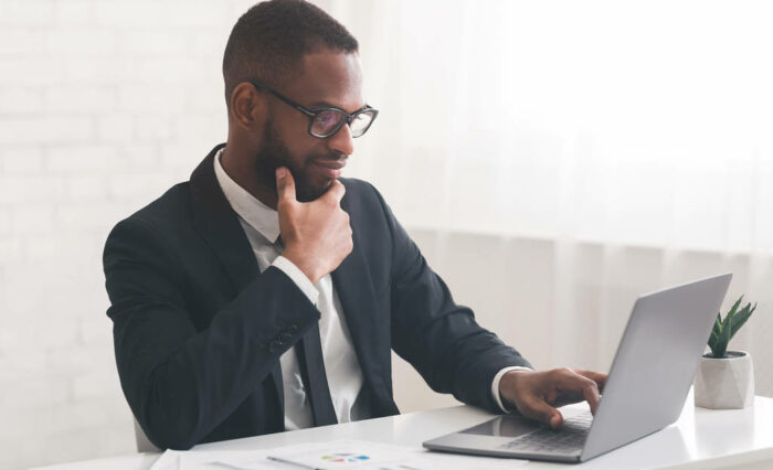 Concentrated afro businessman looking at laptop screen Concentrated black businessman looking at laptop screen, working in office, copy space